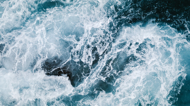 From above aerial view of turquoise ocean water with splashes and foam for abstract natural background and texture