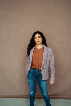 Ethnic female in casual jacket looking at camera standing on brown background in studio