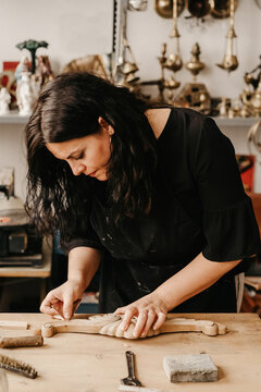 Skilled female artisan polishing decorative carved wooden molding with abrasive paper while working in professional workshop