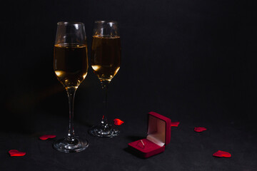 two glasses of champagne stand in the dark, next to a box with a ring to make a marriage proposal, and confetti from hearts