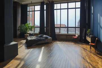 dark interior of a modern stylish huge open-plan loft-style studio apartment with columns and high ceilings. dark blue primed walls are decorated with wood. sunlight enters through huge windows.