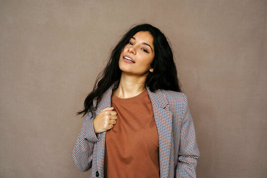 Delighted ethnic female in casual jacket laughing looking at camera on brown background in studio