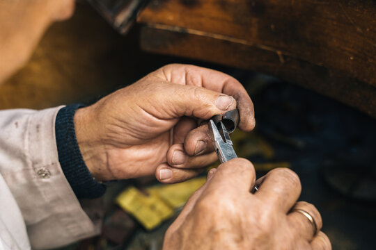 Closeup of crop unrecognizable mature male goldsmith using pliers while working with metal piece and creating jewelry in workshop