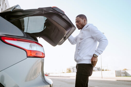 Side view of African American male opening trunk of modern car before driving