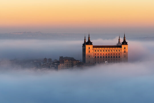 Drone view of peaks of old castles among dense clouds at colorful sunset with hills on horizon in Toledo
