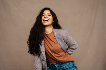 Delighted ethnic female in casual jacket laughing looking at camera on brown background in studio