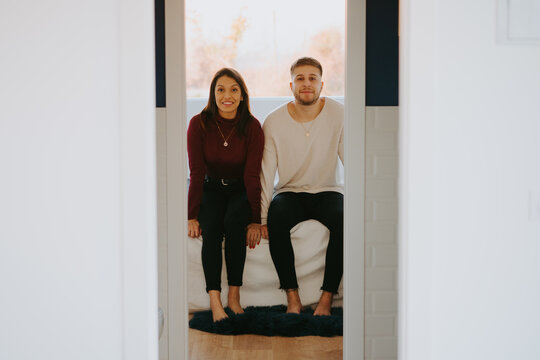 Through opened door of content couple in domestic clothes sitting on soft couch and looking at camera