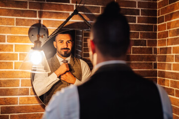 Back view of confident bearded masculine man in formal clothing adjusting tie and looking at reflection in mirror