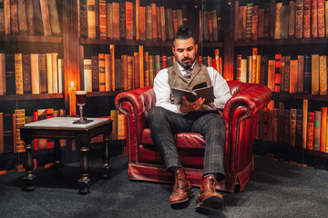 Relaxed bearded male reading book and enjoying liquor while resting on sofa in elegant pub