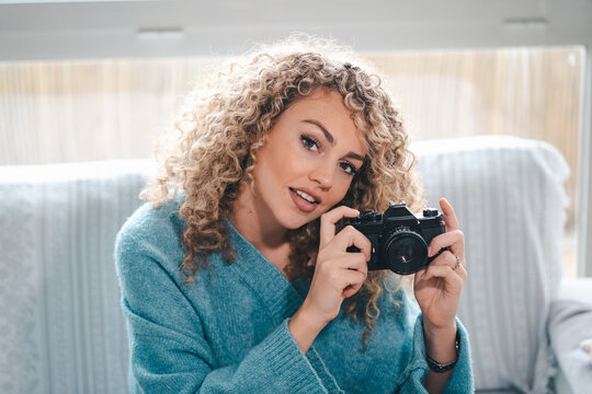 Charming female with curly hair taking picture on photo camera in bright apartment