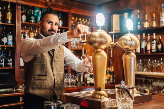 Concentrated adult bearded bartender tapping beer into glass while working at counter in pub - Powered by Adobe