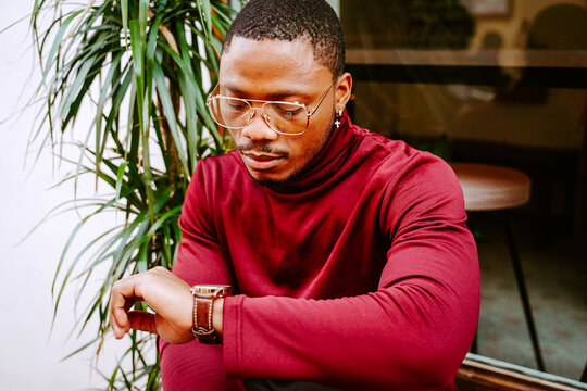 Serious African American male in expensive outfit looking at wristwatch and checking time while waiting for meeting in city