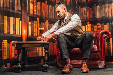 Full body of man in elegant suit holding glass of Irish coffee while resting in comfortable armchair