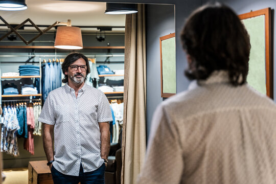 Back view of satisfied man looking at himself in the mirror of a clothing tester in a clothing store