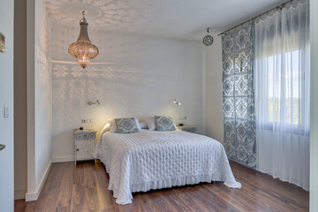 Interior of cozy bedroom with big white bed and classic chandelier hanging from ceiling