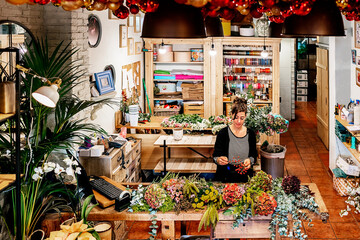 From above professional female florist arranging christmas flower bouquet while working in shop on wooden table