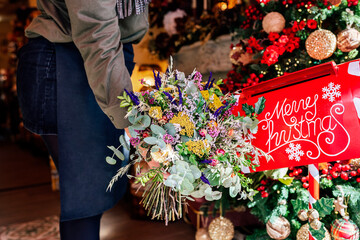 Cropped unrecognizable woman holding flower bouquet standing in shop with christmas decorations near letter box