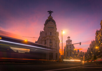 Low angle of blurred light trails in long exposure against Metropolis Building in Madrid at sundown