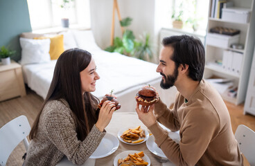 Young couple in love eating hamburgers indoors at home.