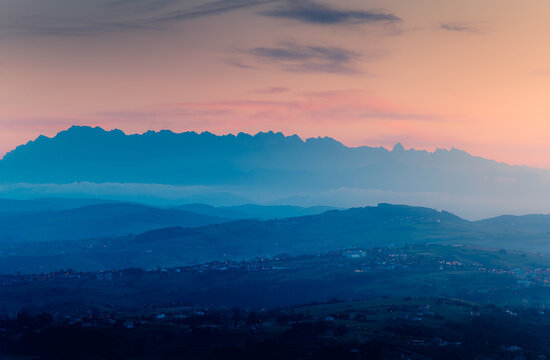 Spectacular scenery of mountains silhouettes with houses located on slopes against pink sunset sky in countryside in Cantabria