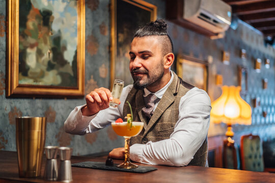 Adult elegant man smelling liquor near tropical cocktail while sitting at counter and resting in bar