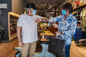 Side view of clothing store owner bumping elbows with customer after shopping while wearing face mask