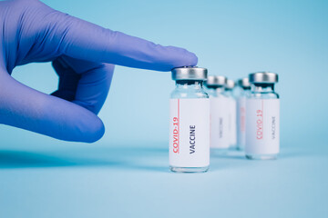Doctor holding vial dose of Covid-19 vaccine against blue background with copy space - prevention coronavirus, global vaccination concept. Comparison of different vaccines. Selective focus