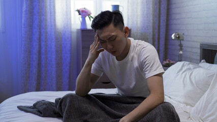 portrait of sickness asian korean male wake up in midnight and sitting on bed massaging his painful head.