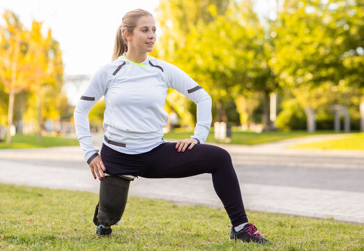 Focused Paralympic female runner with leg prosthesis stretching body and doing forward bend during training