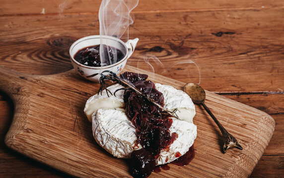High angle of palatable Camembert cheese with cherry jam garnished with rosemary and placed on wooden cutting board