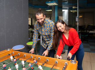 Cheerful young multiethnic people in casual clothes having fun and playing table football together