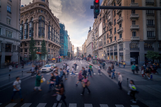 Crowd of blurred unrecognizable pedestrians walking on crosswalk in Madrid city in evening