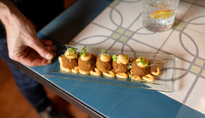 From above of crop anonymous waiter putting tray with delicious deep fried croquettes garnished with cream cheese and herbs on table while serving food in cafe