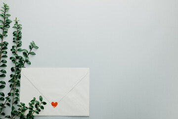 Minimal composition with a white envelope, heart and green leaves