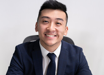 Positive young Asian male executive manager in business style wear looking at camera while sitting in office