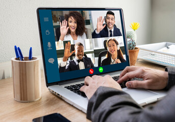 Crop anonymous businessman sitting at table with laptop in office and communicating with multiracial colleagues via video conference