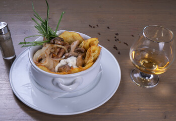 potato pancakes with mushrooms in a pot on a wooden table with cognac baikal