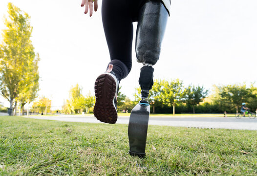 Back view of crop anonymous female runner with leg prosthesis exercising in park during active workout