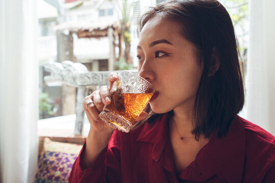 Young Asian female tourist sitting at table set for breakfast and enjoying hot tea while resting in cozy room with traditional oriental items in hotel in Taiwan