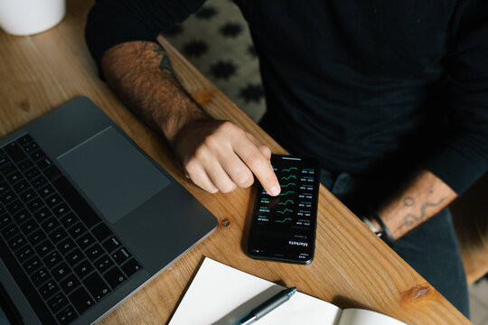 High angle of crop anonymous male entrepreneur using mobile app and working with diagrams at home