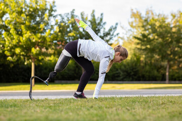 Side view of professional female runner with leg prosthesis preparing for explosive start during training in park