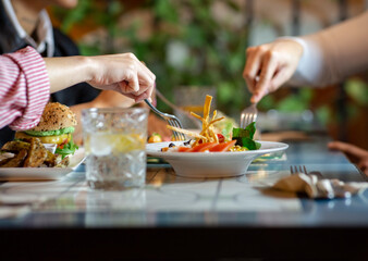 Group of crop anonymous friends gathering at table with various snacks and drinks while having dinner together in cozy restaurant