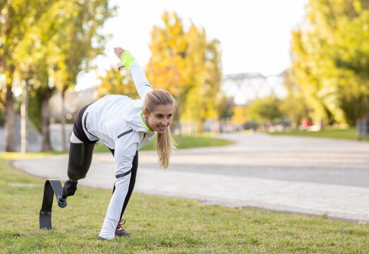Side view of professional female runner with leg prosthesis preparing for explosive start during training in park