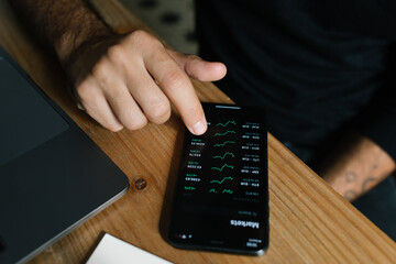 High angle of crop anonymous male entrepreneur using mobile app and working with diagrams at home