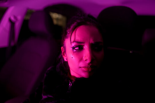 Side view of unhappy young female thinking about problems and crying while driving automobile at night