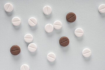 White and brown pills lie on a sheet of gray paper. Close up. Light background or backdrop on the theme of medicine, health care, drugs, pharmacology. Tablets of different colors. Top view. Macro