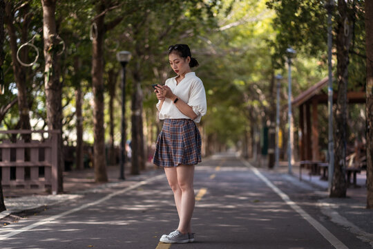 Ethnic Asian female using smartphone and walking along Tanya Shen Green Bikeway in Taichung
