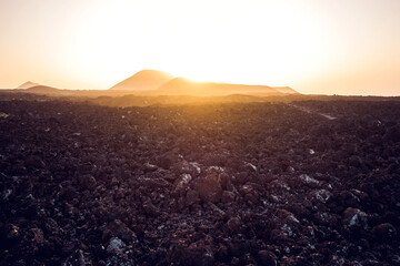 Narrow rough path in volcanic terrain leading to Caldera Blanca and Montana Caldereta craters against cloudless sunset sky in Lanzarote