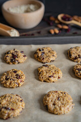 Oatmeal cranberry round cookies before oven, homemade healthy vegan snack or biscuits. Homemade nut bars on baking sheet with ingredients for cooking  on rustic table. Selective focus, copy space