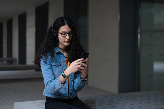 Transgender student with afro hair sitting on a bench while checking her cell phone